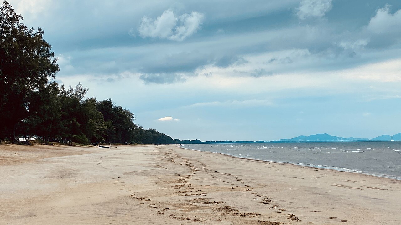 Long sandy shoreline of Sepat Beach lined with trees, hills across the bay